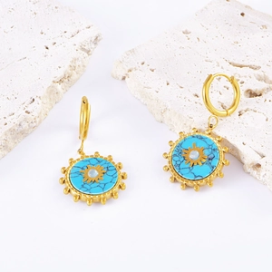 Golden earrings with turquoise discs and sunburst design on textured stone slabs