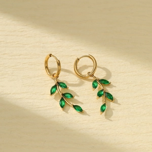 Elegant gold titanium steel leaf earrings with green marquise stones on beige texture