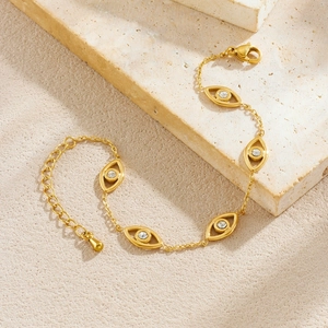 Gold evil eye charm bracelet with crystal accents on a textured natural stone background