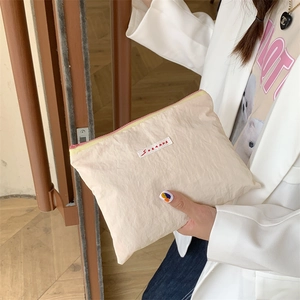 Detail showing hand holding beige nylon makeup bag with red SORAKKA woven label