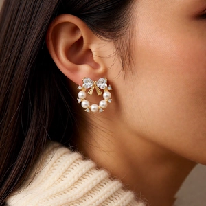 Close-up of pearl wreath earrings with zircon bow on model wearing cream knit sweater