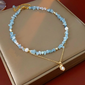 Detail of double-layer necklace with blue aquamarine stones and golden pearl pendant