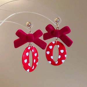 Détail de boucles d'oreilles nœud en velours rouge avec breloques cœur et pois