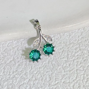 Detailed macro shot of silver cherry pendant with green gemstones and micro-set zircons