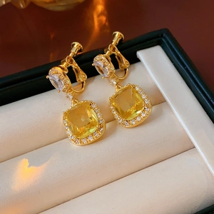Macro shot of 18K gold plated square yellow earrings on a beige velvet jewelry box