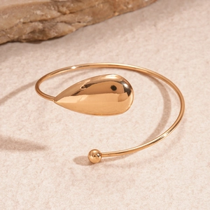 Bracelet de bras minimaliste doré avec détails gouttes et perles sur fond sable