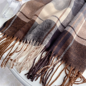 Close-up of the textured brown plaid wool scarf with soft fringe details on a white surface