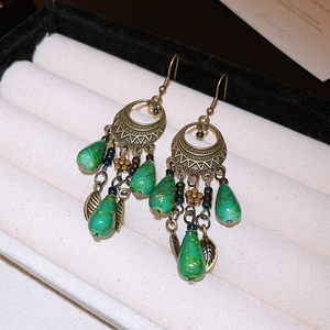 Detail view of retro bronze earrings with green teardrop beads and floral leaf accents