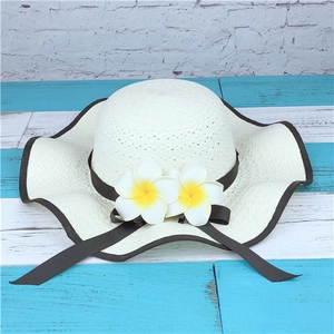 Detail of white wide-brim straw hat with wavy edges and decorative plumeria flowers
