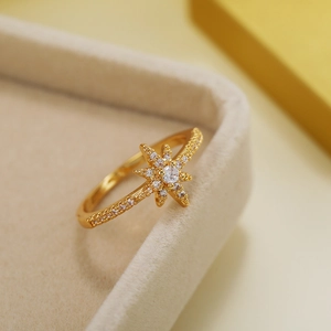 Detailed close-up of a gold-plated starburst ring with clear zircon in a beige jewelry box