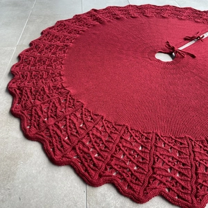Macro detail of red knitted Christmas tree skirt with hollow wavy patterns and ties