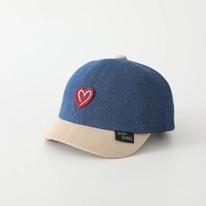 Dettaglio del cappellino in denim bicolore per bambini con ricamo a cuore rosso e visiera corta