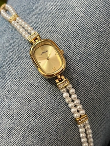 Detail einer eleganten goldenen ovalen Uhr mit Perlenarmband auf blauem Denim-Stoff