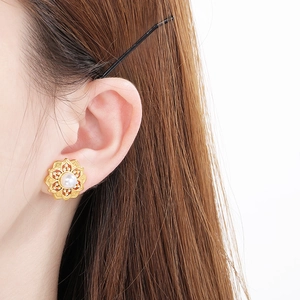 Close-up of elegant gold flower earrings with a white pearl center on a female model