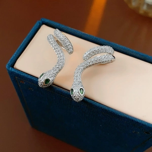Macro view of silver snake earrings with white zircons and green gem eyes on blue velvet