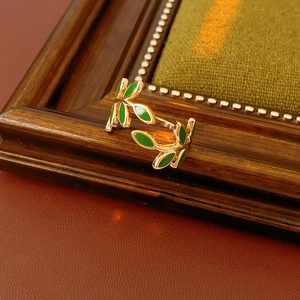 Detail of vintage golden branch ring with green enamel leaves on a wooden frame