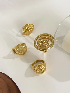 Detail view of four gold stainless steel shell and spiral rings on a white pedestal