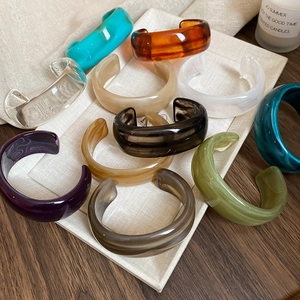 Close-up of colorful irregular resin open bangles displayed on a linen tray background