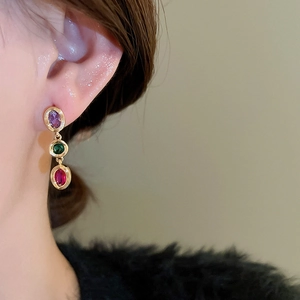 Detail of silver needle drop earrings with three colorful oval zircons on female ear