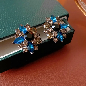 Dettaglio di orecchini vintage a fiore con strass blu e neri su una scatola per gioielli