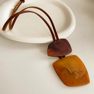Detailed shot of amber and tan irregular resin pendant on brown suede cord necklace