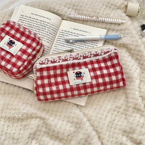 Macro detail of red plaid wool pouches with white lace trim on a soft fleece background