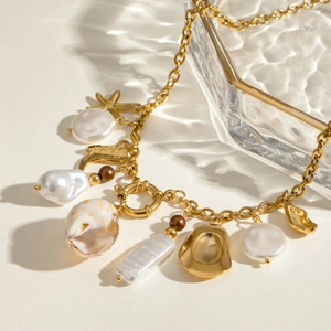 Detail of gold chain necklace with shell pendants and irregular pearls on textured background