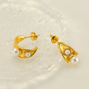Détail de boucles d'oreilles dorées en C avec perles blanches et texture ciselée