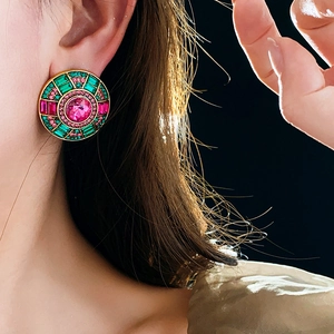 Macro view of vintage round gold stud earrings with pink and green crystal gems on model
