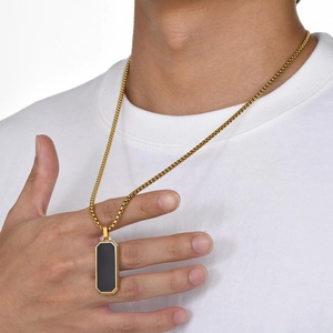 Nahaufnahme einer Herren-Goldkette mit rechteckigem schwarzem Anhänger an einem Modell