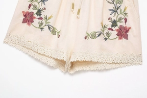Detail of floral embroidery and crochet lace trim on beige knit drawstring shorts