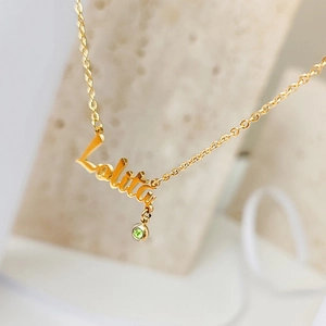 Macro shot of custom Lolita name necklace in gold with a green birthstone charm