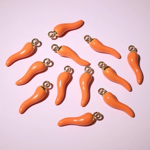 Detailed top view of orange chili pendants with golden loops on pink background