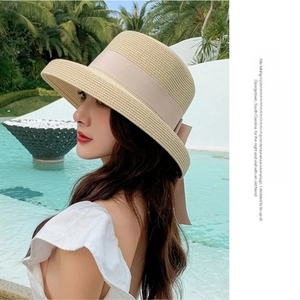 Detail of hand-woven straw sun hat featuring a wide brim and soft pink ribbon bow