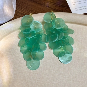 Detail of mint green layered disc drop earrings on a beige tray with gold hardware