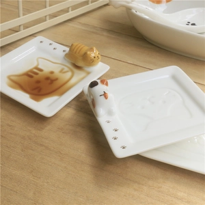 Close-up of ceramic sauce dish with 3D cat relief and embossed pattern on wood table