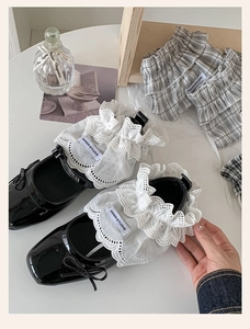 Detail of white lace ankle cuffs with grey plaid accents paired with black patent shoes