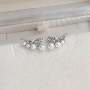 Macro detail of silver curved earrings with white pearls and blue zircon accents