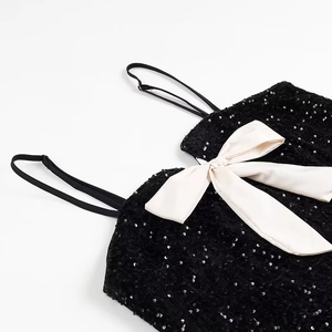 Detailed close-up of a black sequin top featuring a large cream satin bow decoration