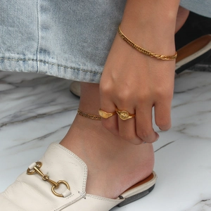 Detailed view of gold chain set with signet rings and bracelets on light denim outfit