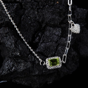 Macro shot of silver emerald green gemstone necklace with asymmetric heart link chain