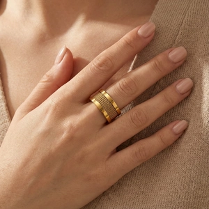 Close-up of golden mesh woven stainless steel ring on finger with beige sweater background
