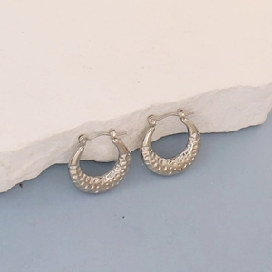 Detail of silver oval hoop earrings with hammered texture on a marble surface