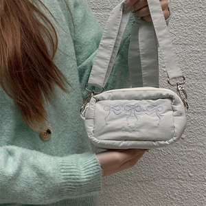 Detail of light blue crossbody bag featuring three white embroidered bows and wide strap