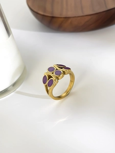 Detailed shot of golden ring featuring purple enamel oval elements on a white surface