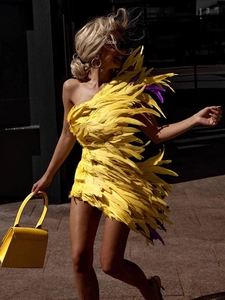 Détail de la robe mini jaune à une épaule avec garniture en plumes et coupe ajustée chic