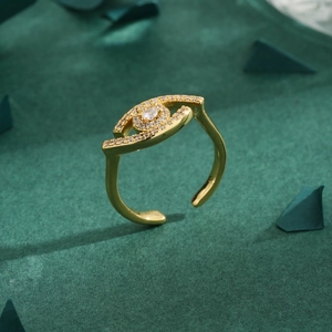 Golden eye-shaped ring with clear zirconia stones on a dark green textured background