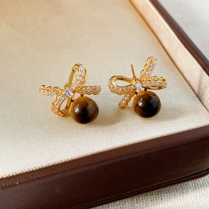 Macro shot of gold bow earrings with zircon and tiger eye stones in a velvet jewelry box