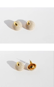 Detail view of round beige enamel stud earrings with gold drop accents and metal posts