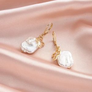 Detail of baroque pearl drop earrings with golden cross pendants on pink silk fabric